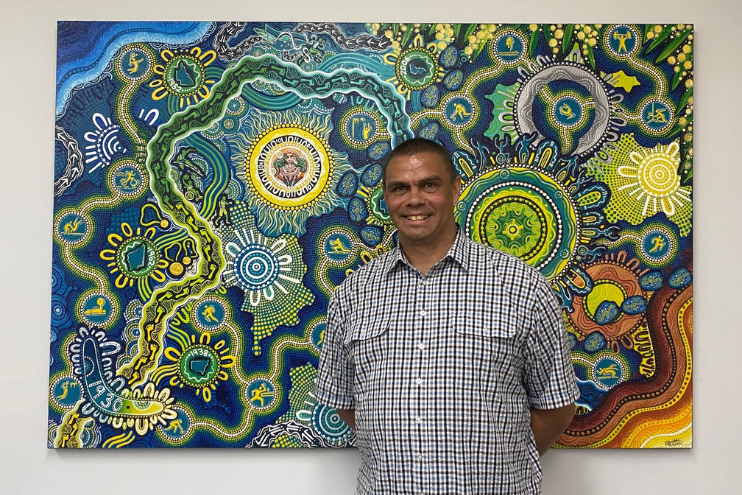 Kyle Vander-Kuyp, Chair of the Reconciliation Action Plan Advisory Group, in front of Commonwealth Games Australia's RAP Artwork