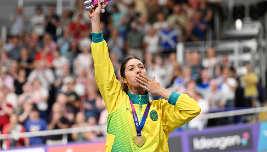 Female athlete in a yellow-green jersey raises a trophy and kisses her medal amid a cheering crowd.
