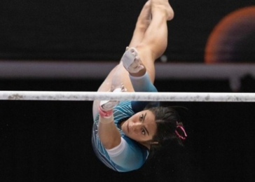Gymnast on the uneven bars, upside down, wearing a blue leotard with white sleeves and chalk on her hands.