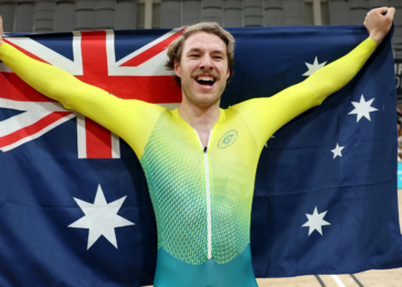Athlete celebrates victory, arms raised while holding the Australian flag in a sports arena