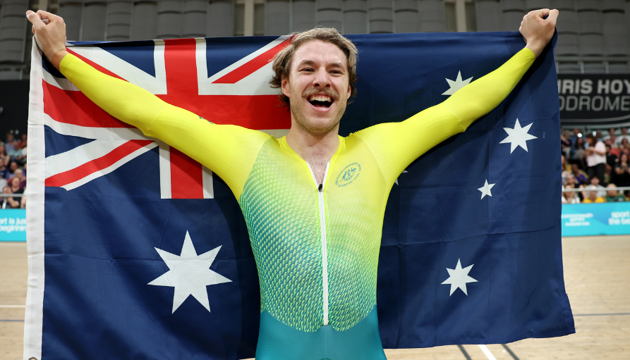 Athlete celebrates victory, arms raised while holding the Australian flag in a sports arena