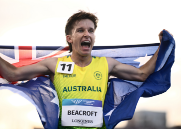 Australian sprinter Beacroft finishes race, arms raised, draped in the Australian flag.