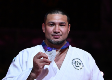 Male judoka in a white gi holding a silver medal at a competition.