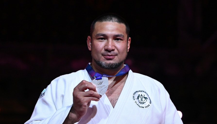 Male judoka in a white gi holding a silver medal at a competition.