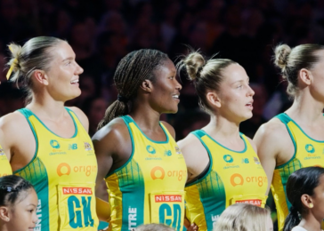 Group of female athletes in yellow-green uniforms standing together on a podium, smiling and looking to the side.