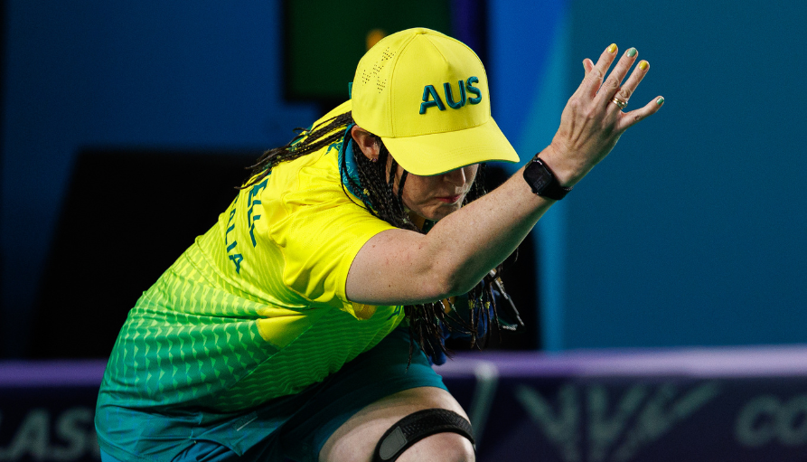 Australian athlete in a bright yellow cap and jersey reaching forward during a match.