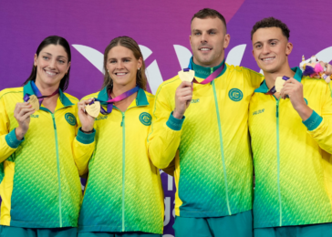 Four athletes in bright yellow-green tracksuits pose with gold medals against a purple backdrop, smiling at the camera.