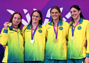 Four female athletes in yellow-green jackets pose with gold medals on a purple backdrop.
