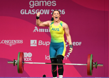 Australian female weightlifter on a pink Glasgow 2016 stage, lifting a loaded barbell and celebrating victory.