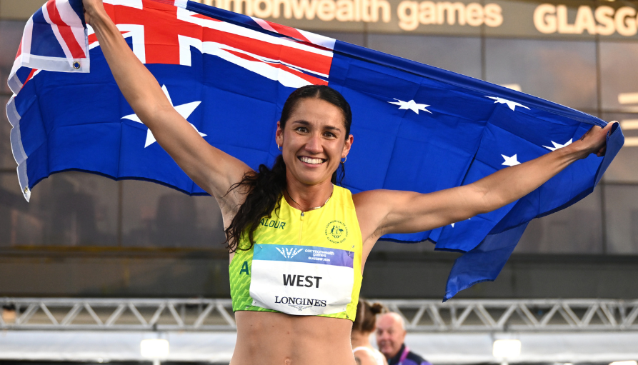 Smiling female athlete in a yellow top raises an Australian flag in celebration at the Commonwealth Games.